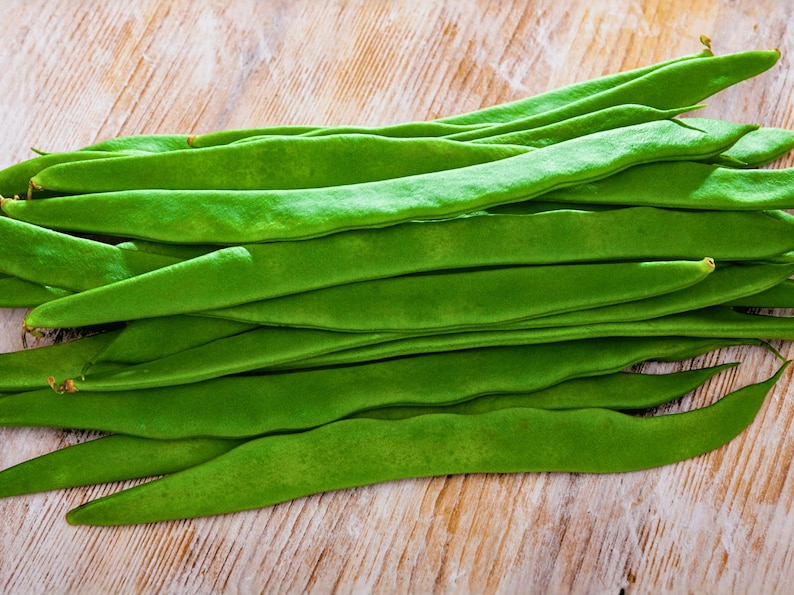 A pile of fresh green beans is neatly arranged on a wooden surface.