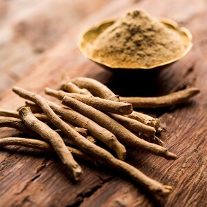 a pile of dried Ashwagandha roots on a wooden surface, with a small bowl containing a golden-colored powder or spice next to it.