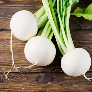 May include: Three white turnips with green leafy tops on a brown wooden surface.