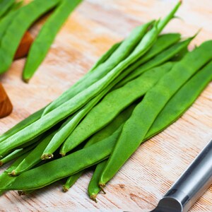 A pile of fresh green beans is displayed on a wooden surface, with a knife nearby.