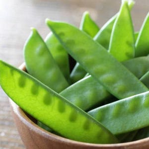 May include: A bowl filled with fresh, green snow peas. The peas are arranged in a cluster, with some overlapping.