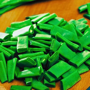 May include: A close-up shot of freshly cut green beans on a wooden cutting board. The beans are bright green and appear to be recently sliced. The wooden board has a warm, natural tone, providing a contrast to the vibrant green vegetables.