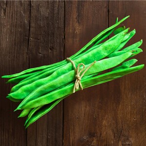 A bundle of fresh green beans tied with a string, resting on a wooden surface.