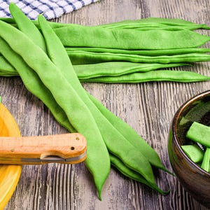 a variety of fresh green beans on a wooden surface, including whole beans and cut pieces. A knife is also visible, suggesting that the beans have been recently prepared.