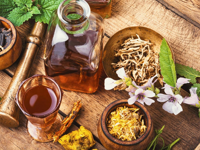 various Medicinal Marshmallow herbs, spices, and a glass of liquid on a wooden surface, suggesting a collection of natural ingredients or a display of culinary items.