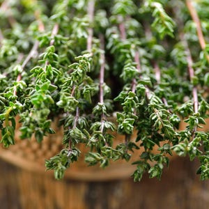 May include: A bunch of fresh green thyme sprigs in a woven basket. The thyme is a popular herb used in cooking.
