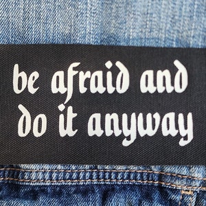 Może przedstawiać: Czarna kurtka dżinsowa z białą naszywką z napisem "be afraid and do it anyway".