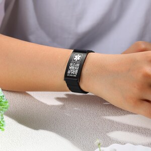 May include: Black medical ID bracelet with a white emergency symbol and QR codes. The bracelet has the text "HEALTH INFO" and "SCAN ME". The bracelet is worn on a wrist.