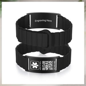 Könnte beinhalten: Schwarzes medizinisches Armband mit strukturiertem Band und Metallplatte. Die Platte trägt auf der einen Seite die Aufschrift "Gravur hier" und auf der anderen Seite ein medizinisches Symbol, einen QR-Code sowie den Text "Health Info" und "Scan Me".