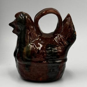 May include: A white ceramic mug with a black handle and the text "But First, Coffee" in a bold, black font. The mug is set against a blurred background, suggesting a cozy setting.