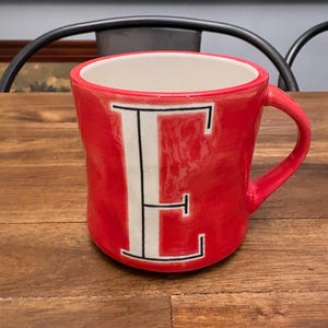 May include: A white ceramic mug with a black handle and the text "But First, Coffee" in a black, bold font. The mug is on a white surface. The mug is approximately 4 inches tall.