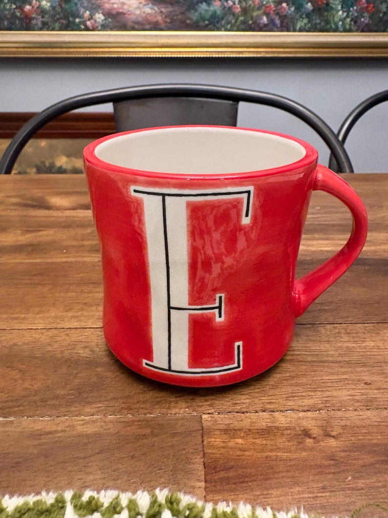 May include: A white ceramic mug with a black handle and the text "But First, Coffee" in a black, bold font. The mug is on a white surface. The mug is approximately 4 inches tall.