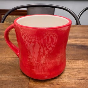 May include: A set of three ceramic mugs with a speckled, cream-colored glaze. Each mug features a different hand-painted floral design in shades of blue, green, and yellow. The mugs have a simple, rounded shape and a comfortable handle.