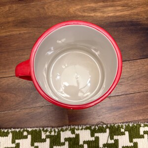 May include: A white ceramic mug with a black handle and the text "But First, Coffee" in a bold, black font. The mug is sitting on a wooden surface. The mug is approximately 4 inches tall.