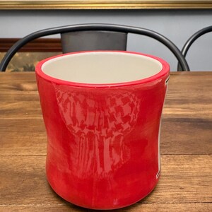 May include: A white ceramic mug with a black handle and the text "But first, coffee" in a handwritten style. The mug is on a white surface. The mug is approximately 4 inches tall.