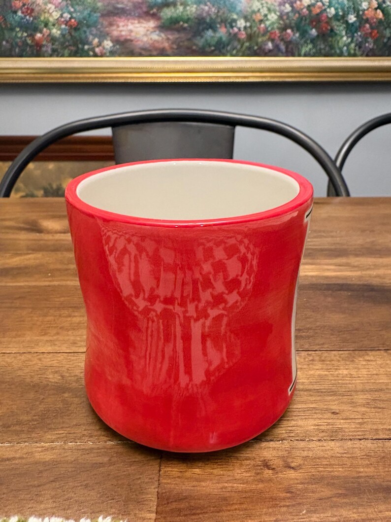 May include: A white ceramic mug with a black handle and the text "But first, coffee" in a handwritten style. The mug is on a white surface. The mug is approximately 4 inches tall.