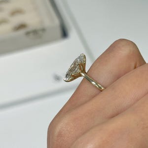 Op de afbeelding: Een gouden ring met een grote, marquise-geslepen diamant. De diamant is gezet in een vier-klauwzetting en de band is van eenvoudig, gepolijst goud. De ring wordt op een vinger getoond, met een vage achtergrond.