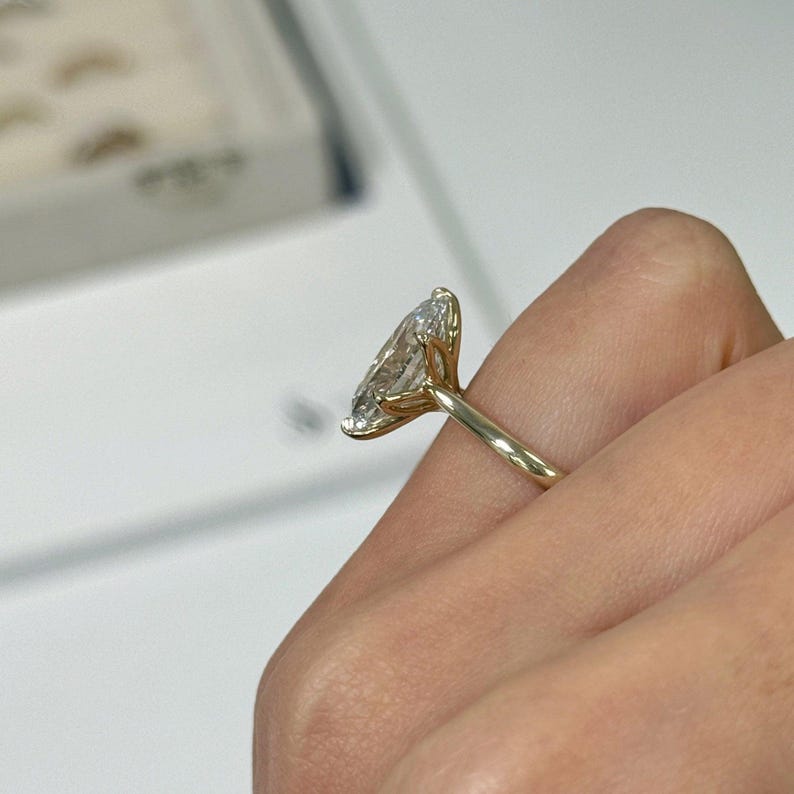 Op de afbeelding: Een gouden ring met een grote, marquise-geslepen diamant. De diamant is gezet in een vier-klauwzetting en de band is van eenvoudig, gepolijst goud. De ring wordt op een vinger getoond, met een vage achtergrond.