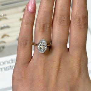 Op de afbeelding: Een gouden verlovingsring met een grote, ovaal geslepen diamant. De diamant is het middelpunt, gezet op een fijne gouden band. De ring wordt getoond op een vinger, waarbij de schittering en het ontwerp worden benadrukt.