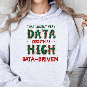 May include: A light gray hooded sweatshirt featuring the text "THAT WASN'T VERY DATA CHRISTMAS HIGH DATA-DRIVEN" printed on the front. The words "DATA" and "HIGH" are in a large, stylized green font with red outlines, while the other text is red.