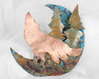 Op de afbeelding: Een koperen wolfsilhouet dat huilt naar de maan, met twee koperen bomen erachter. De maan en de bomen hebben een blauwe en groene patina.