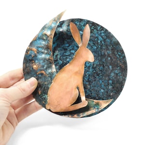 K&ouml;nnte beinhalten: Eine Kupfer-Wanddekoration mit einer Sichelmondform und einer stilisierten Hasensilhouette. Der Mond ist mit einer blauen und gr&uuml;nen Patina texturiert.