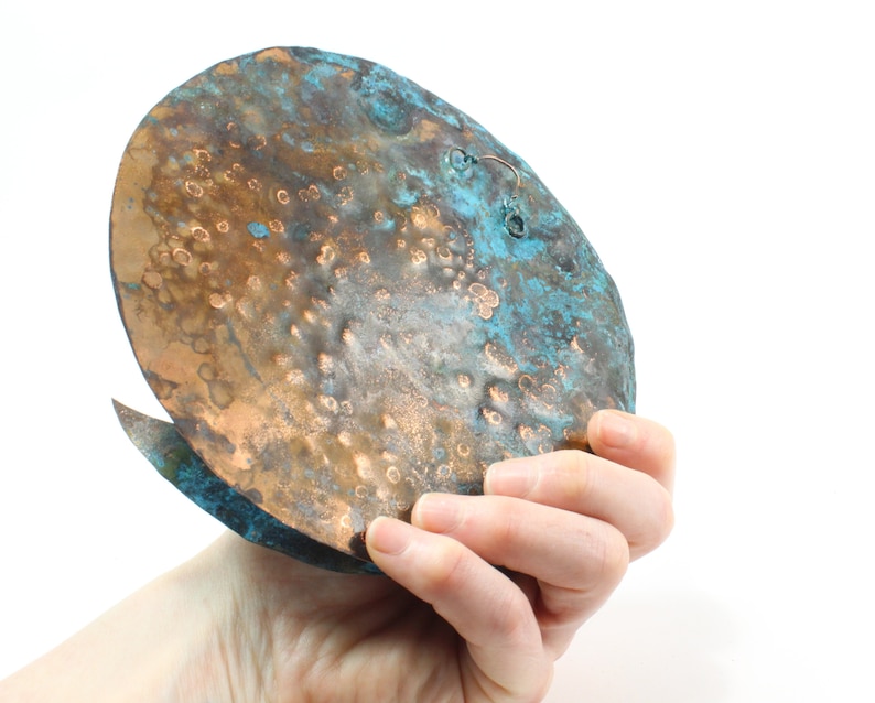 K&ouml;nnte beinhalten: Ein geh&auml;mmerter Kupfer-Wandbehang mit einer blaugr&uuml;nen Patina. Das St&uuml;ck hat eine abgerundete Form und eine strukturierte Oberfl&auml;che.