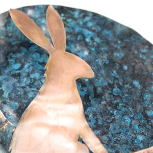 K&ouml;nnte beinhalten: Eine Kupfersilhouette eines Kaninchens, das auf einem Halbmond sitzt. Der Mond ist aus Kupfer und hat eine blaue und gr&uuml;ne Patina.
