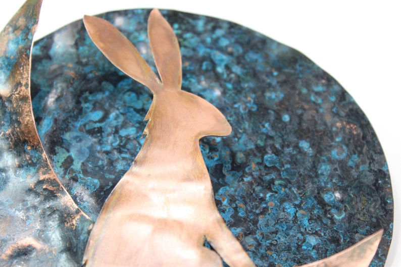 K&ouml;nnte beinhalten: Eine Kupfersilhouette eines Kaninchens, das auf einem Halbmond sitzt. Der Mond ist aus Kupfer und hat eine blaue und gr&uuml;ne Patina.
