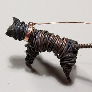 May include: A wire sculpture of a dog with a copper collar and a tag that reads "1112". The dog is made of twisted wire and has a long tail.