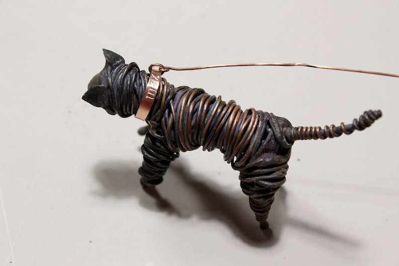 May include: A wire sculpture of a dog with a copper collar and a tag that reads "1112". The dog is made of twisted wire and has a long tail.