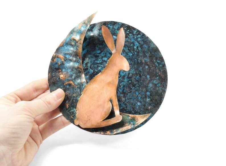 K&ouml;nnte beinhalten: Eine Kupfer-Wanddekoration mit einer Sichelmondform und einer stilisierten Hasensilhouette. Der Mond ist mit einer blauen und gr&uuml;nen Patina texturiert.