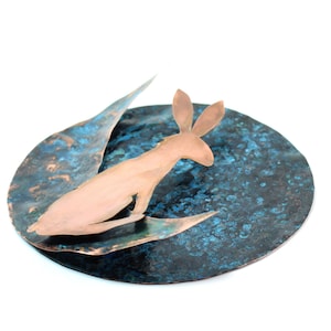 K&ouml;nnte beinhalten: Eine Kupferskulptur eines Kaninchens auf einer blauen und kupferfarbenen, strukturierten Scheibe.