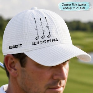 May include: White golf cap with a textured pattern. The cap features the name "ROBERT" on the side and the phrase "BEST DAD BY PAR" with golf club graphics. Additional text includes "Custom Title, Names And Up To 20 Kids".
