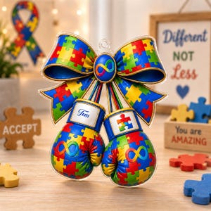May include: A decorative ornament featuring two miniature boxing gloves suspended from a large bow. The gloves and bow are patterned with a colorful jigsaw puzzle design. One glove displays the name Tom, while both feature a rainbow infinity symbol.