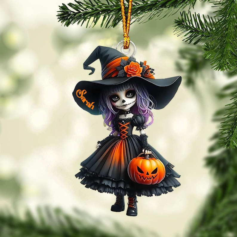 May include: A Halloween-themed ornament featuring a witch doll with a black hat, orange and black dress, and a pumpkin. The doll's face is painted with a skull design and the name "Sarah" is written on the hat.