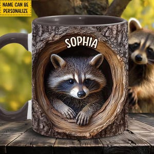 Può includere: Una tazza in ceramica bianca con manico nero presenta un procione che spunta da un tronco d'albero. La tazza ha il nome "Sophia" stampato su di essa.