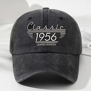 May include: A dark gray baseball cap with the text "Classic 1956 Limited Edition" embroidered in white. The cap has a curved brim and a button on top. The hat is made of a soft, worn material.