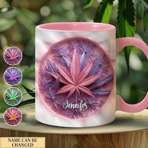 Op de afbeelding: Een roze keramische mok met een wit ontwerp van een roze marihuanablad omringd door paarse bloemen. De naam "Jennifer" staat in een cursief schrift onder het blad.