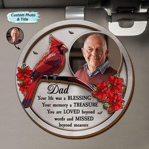 Pode incluir: Um ornamento de carro redondo, prateado, com um pássaro cardeal vermelho empoleirado em um galho. O ornamento tem uma moldura para foto com um retrato de homem e o texto "Pai, Sua vida foi uma BÊNÇÃO, Sua memória um TESOURO, Você é AMADO além das palavras e SENTIDO FALTA além de toda medida."