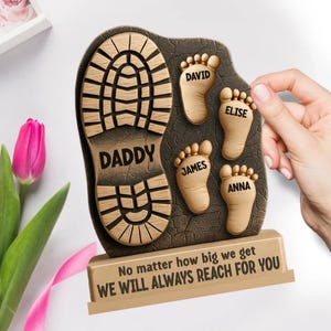 May include: A wooden plaque featuring a boot print with the word "DADDY" and four small footprints with names. The plaque includes the text "No matter how big we get, WE WILL ALWAYS REACH FOR YOU."