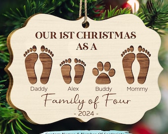 May include: A wooden Christmas ornament with the text "Our 1st Christmas as a Family of Four - 2024 -" and four sets of footprints, including a paw print. The ornament is decorated with a brown wood grain pattern.