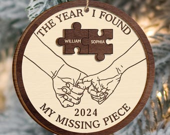 May include: A round wooden bauble with a beige background and brown trim. The bauble features a couple's names, "William" and "Sophia", on two jigsaw pieces that fit together. The text "The year I found my missing piece" surrounds the jigsaw pieces, and the year "2024" is centred below.