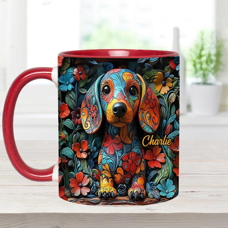 Puede incluir: Una taza de caf&eacute; de cer&aacute;mica roja y blanca con una ilustraci&oacute;n colorida de un perro salchicha con patrones florales. El nombre del perro, "Charlie", est&aacute; escrito en texto amarillo en la taza.