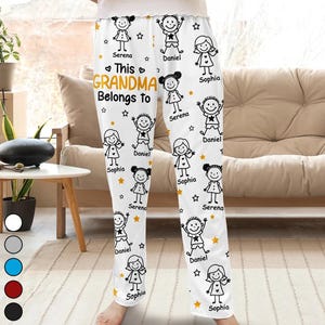 May include: White pajama trousers featuring a repeating pattern of cartoon children, stars, and the text "This Grandma Belongs To" with names. The trousers have a comfortable, relaxed fit.