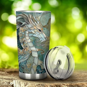 May include: A stainless steel tumbler with a lid and a colourful stained glass design of a dragon. The tumbler has the name "Jennifer" printed on it.
