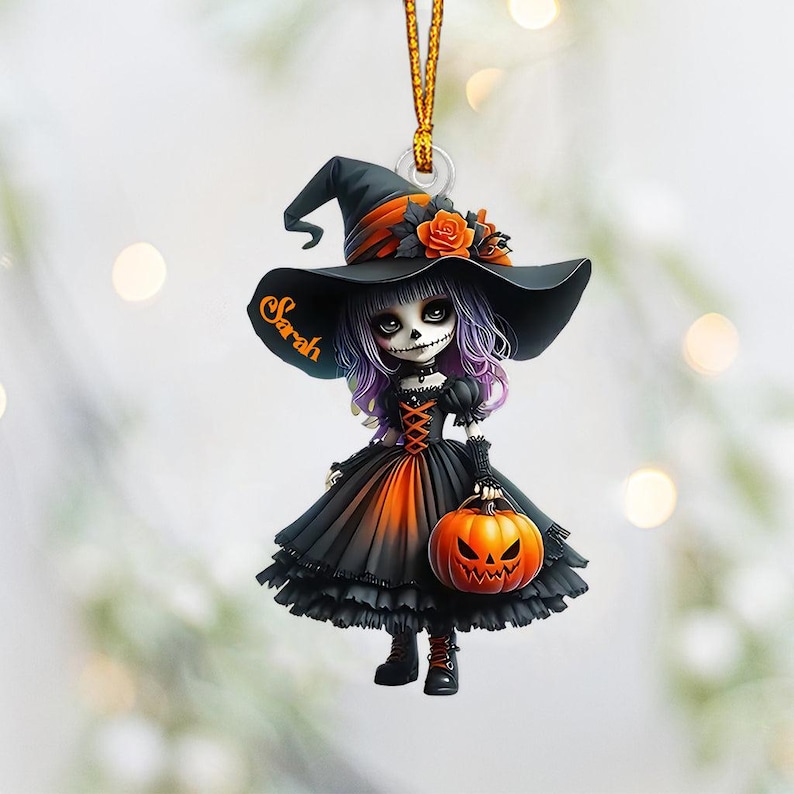 May include: A black and orange Halloween ornament featuring a witch doll with a black hat, purple hair, and a black and orange dress. The doll is holding a jack-o-lantern and the hat has the name "Sarah" written on it.