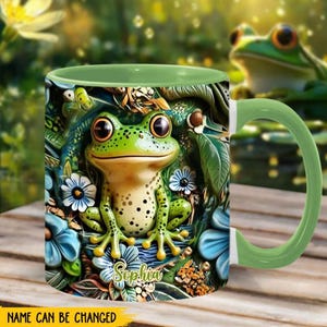 Puede incluir: Una taza de cerámica verde con un diseño de rana verde y flores. La taza tiene un asa verde y el nombre "Sophia" está impreso en la parte delantera.
