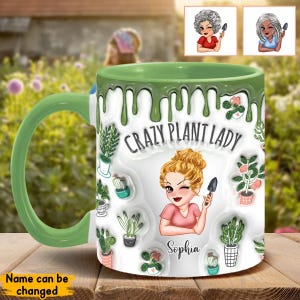 Op de afbeelding: Een witte keramische mok met een groene rand en handvat. De mok heeft een groen druppelontwerp en bevat een cartoonillustratie van een vrouw met blond haar die een tuinschep houdt. De mok zegt "Crazy Plant Lady" en heeft de naam "Sophia" onder de illustratie.