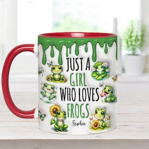 May include: A white ceramic mug with a red rim and green dripping paint design. It features a cartoon frog design and the text "Just a girl who loves frogs" with the name "Sophia" at the bottom.